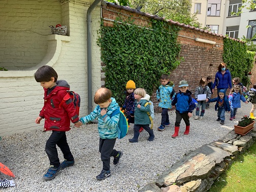 Children holding hands walking two by two in the garden.