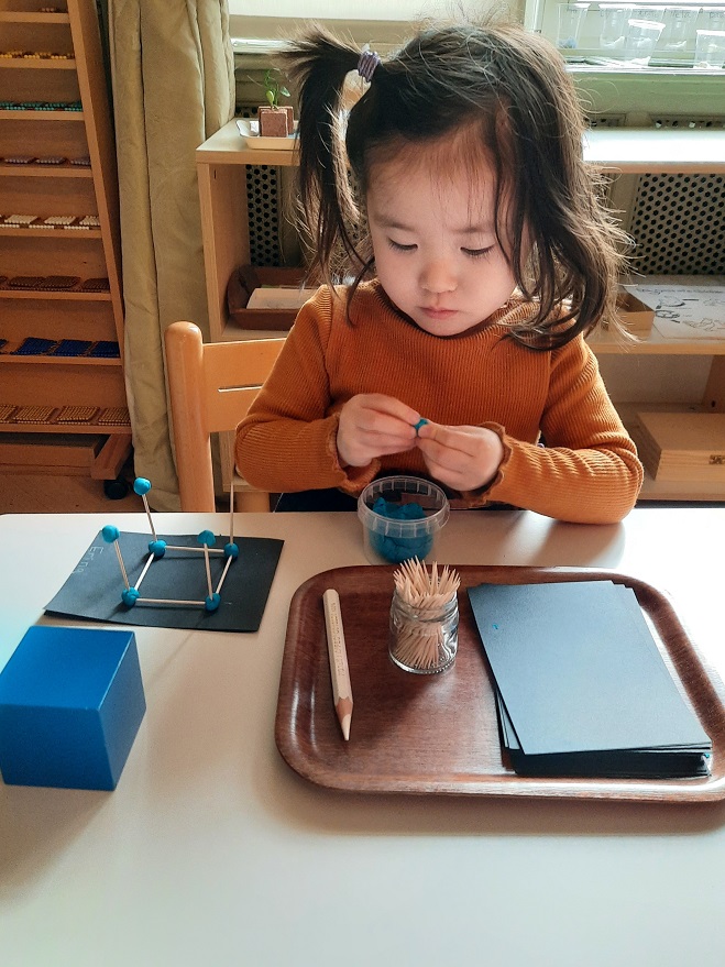 A young girl creating a shape with playdough and matchsticks.