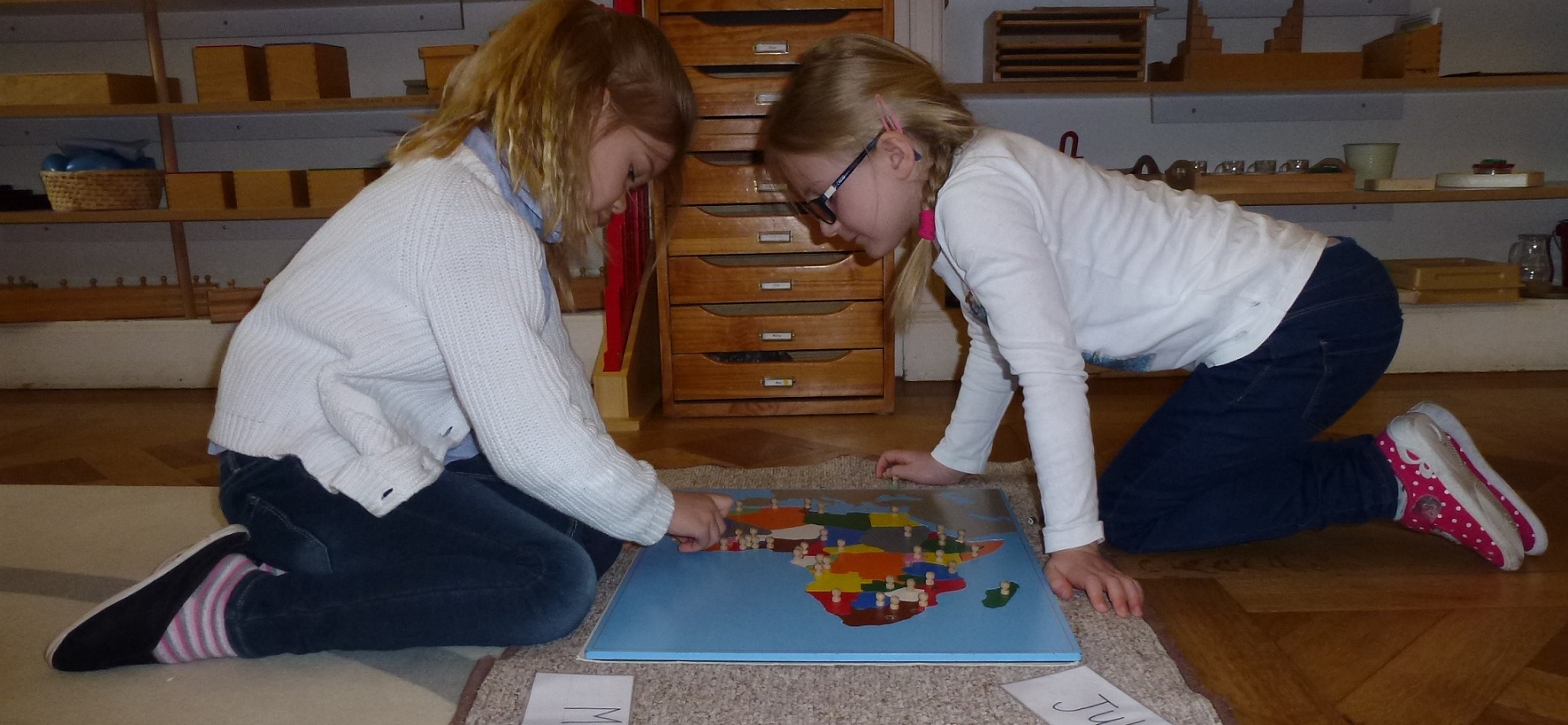 Two children working on the floor to match the country shapes in a map of Africa using Montessori materials.