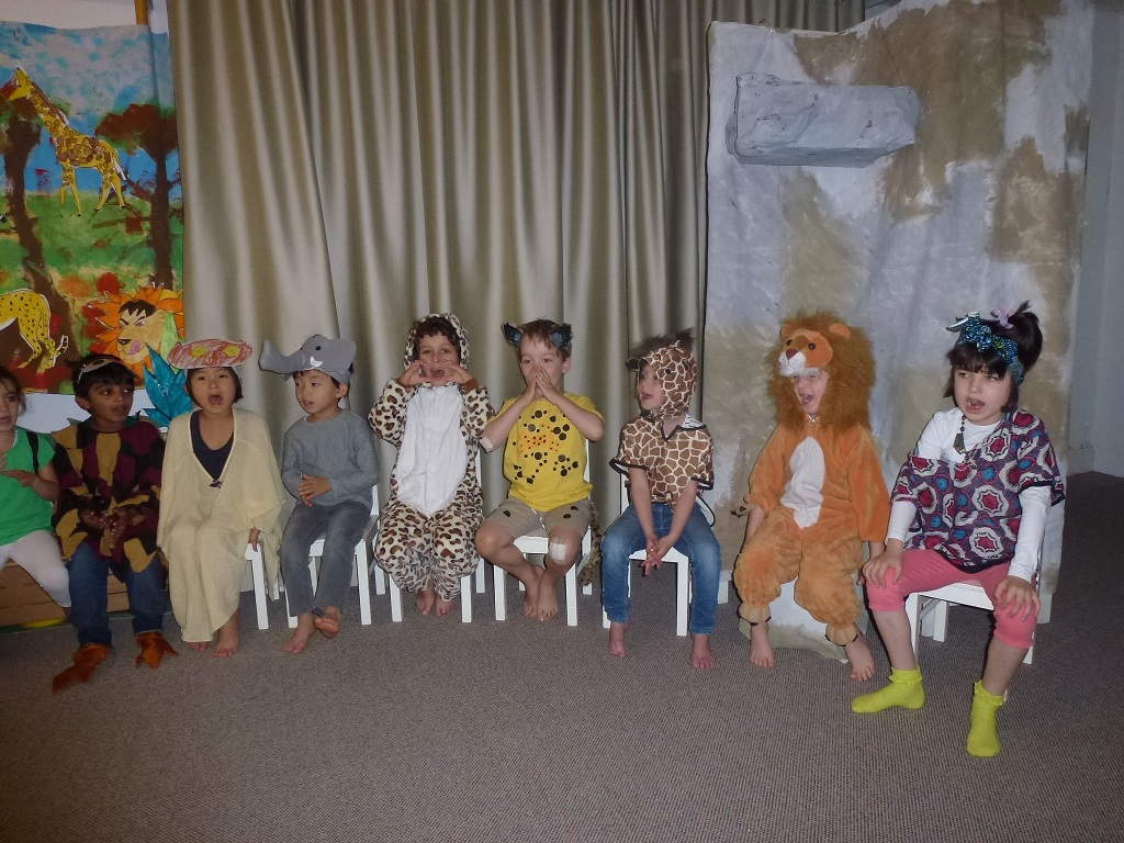 Children in different costumes sitting on chairs and giving a performance.