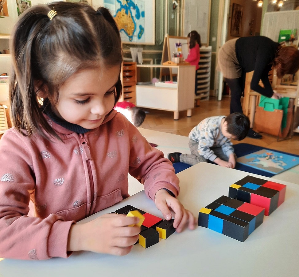 Child using geometric shapes on a table in primary at Montessori House Brussels