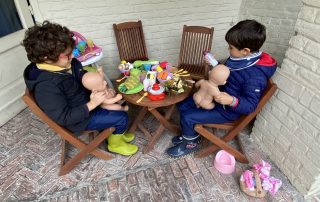 Two young boys playing with dolls at a table in the garden.