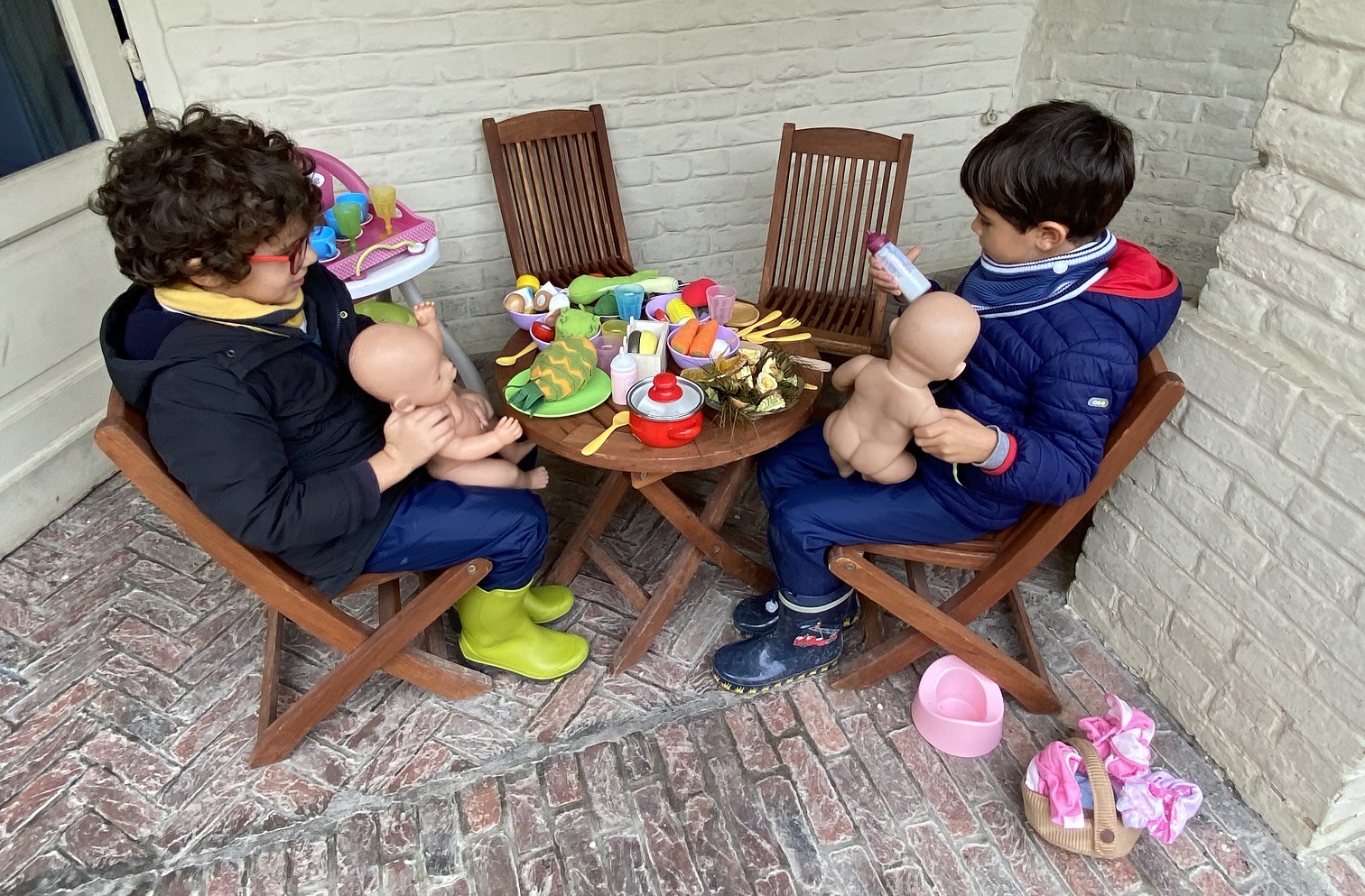 Two young boys playing with dolls at a table in the garden.
