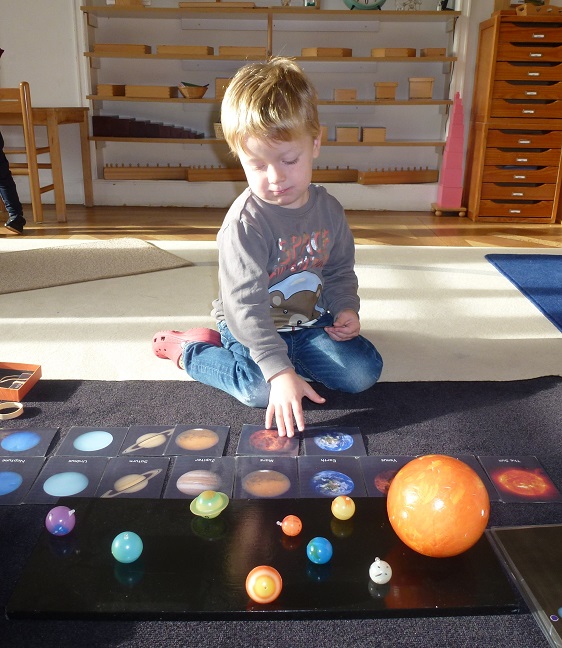 A child sitting on the floor learning about the shapes and colours of each planet.