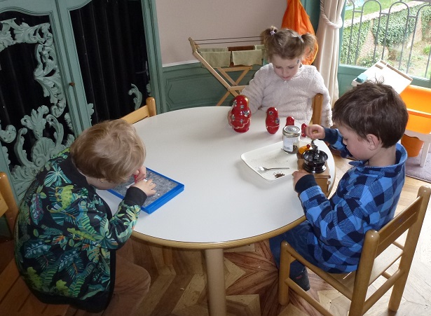 Three children are sitting at a table, each doing activities totally independently.