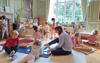 A Montessori guide is observing children carrying out their various activities in the classroom.