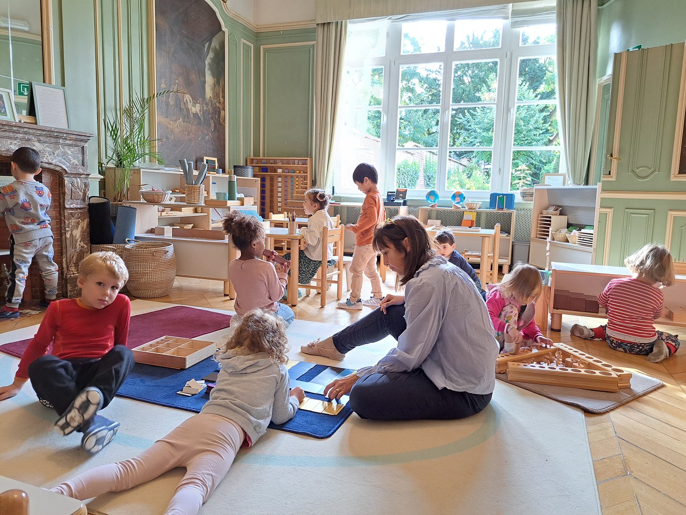 A Montessori guide is observing children carrying out their various activities in the classroom.